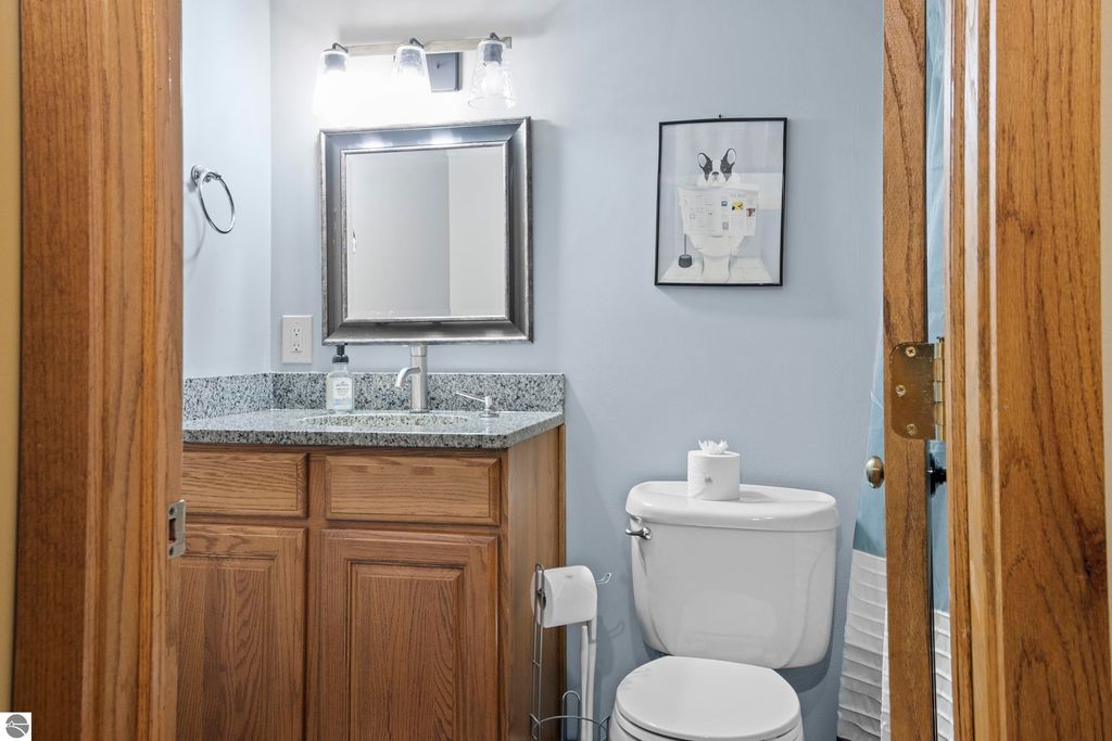 Modern bathroom with wooden cabinetry, granite countertop, mirror, and decorative wall art, featuring a toilet and towel rack, set in a serene blue color scheme.
