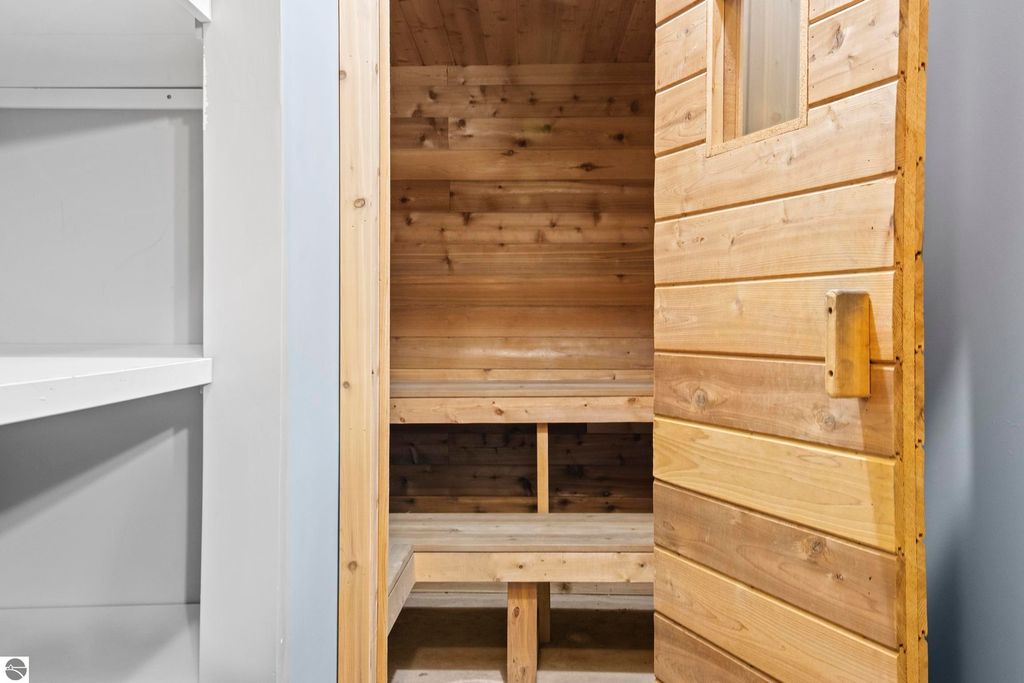 Sauna interior with wooden benches and door, showcasing a relaxing feature of the Traverse City home at 10371 Deerpath North.