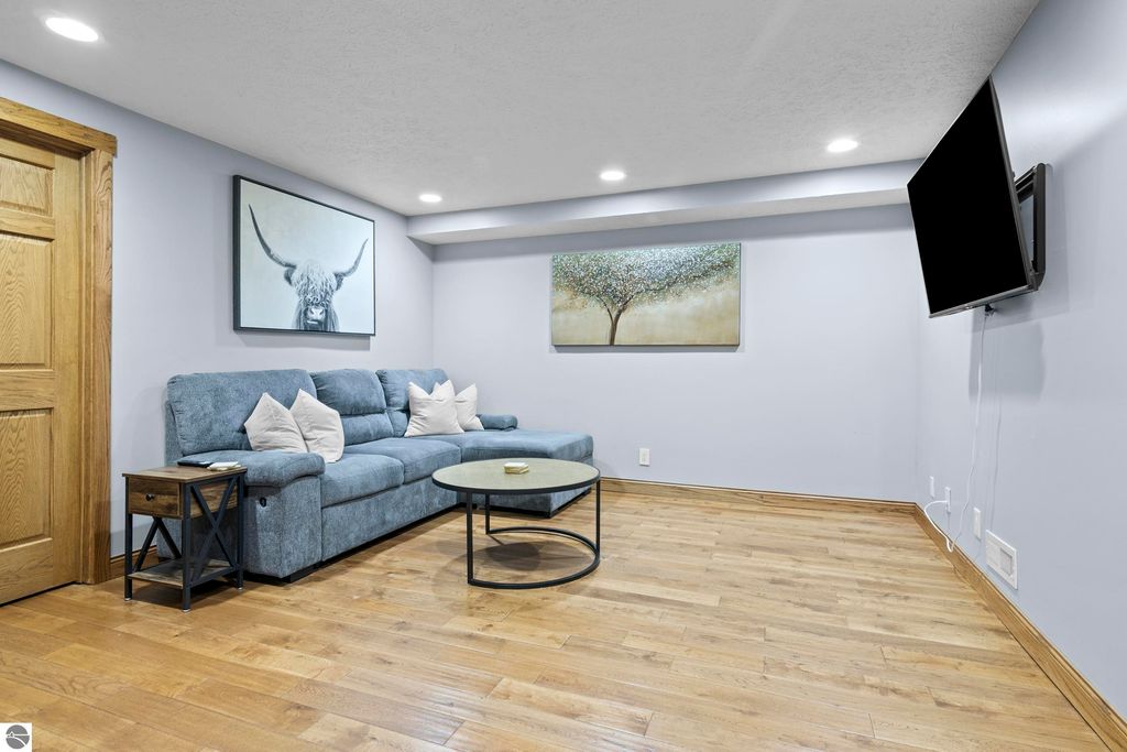 Cozy living room featuring a blue sectional sofa with decorative pillows, a round coffee table, wall-mounted TV, and artwork, set against light blue walls and hardwood flooring.