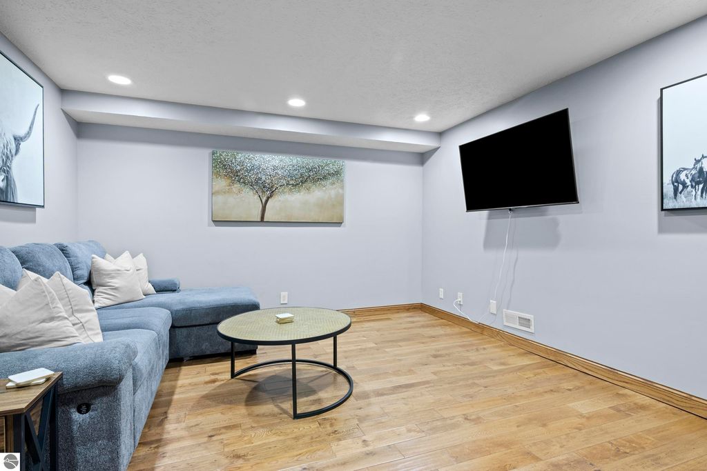 Cozy living area featuring a blue sectional sofa with decorative pillows, round coffee table, wall-mounted TV, and art pieces including a tree painting and animal artwork, showcasing modern interior design in a spacious layout.
