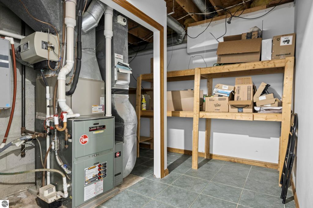 Utility room featuring a Rheem furnace, storage shelving with boxes, and exposed ductwork, showcasing functional space in the Traverse City home at 10371 Deerpath North.