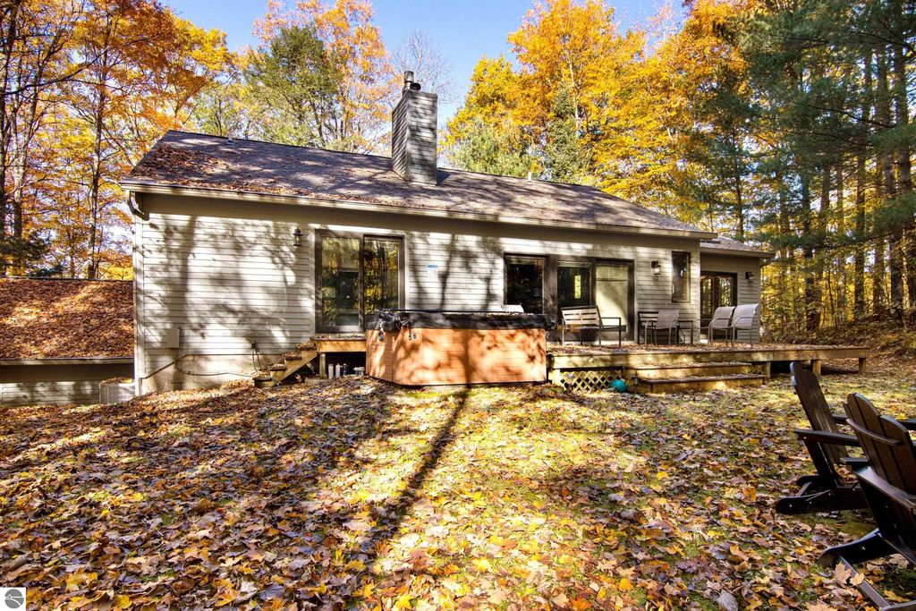 Back view of a modern home with a spacious deck, hot tub, and outdoor seating, surrounded by colorful autumn foliage, located on wooded property in Traverse City, MI.