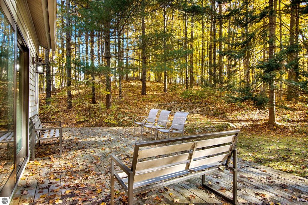 Wooden deck with seating overlooking a wooded area in autumn, showcasing vibrant fall foliage, complementing the serene lifestyle offered by the property at 10371 Deerpath North, Traverse City, MI.