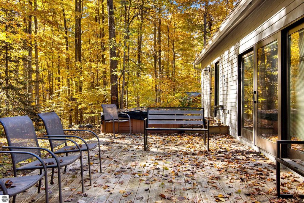 Deck area with seating and a hot tub surrounded by colorful autumn foliage, showcasing outdoor living space at 10371 Deerpath North, Traverse City, MI.
