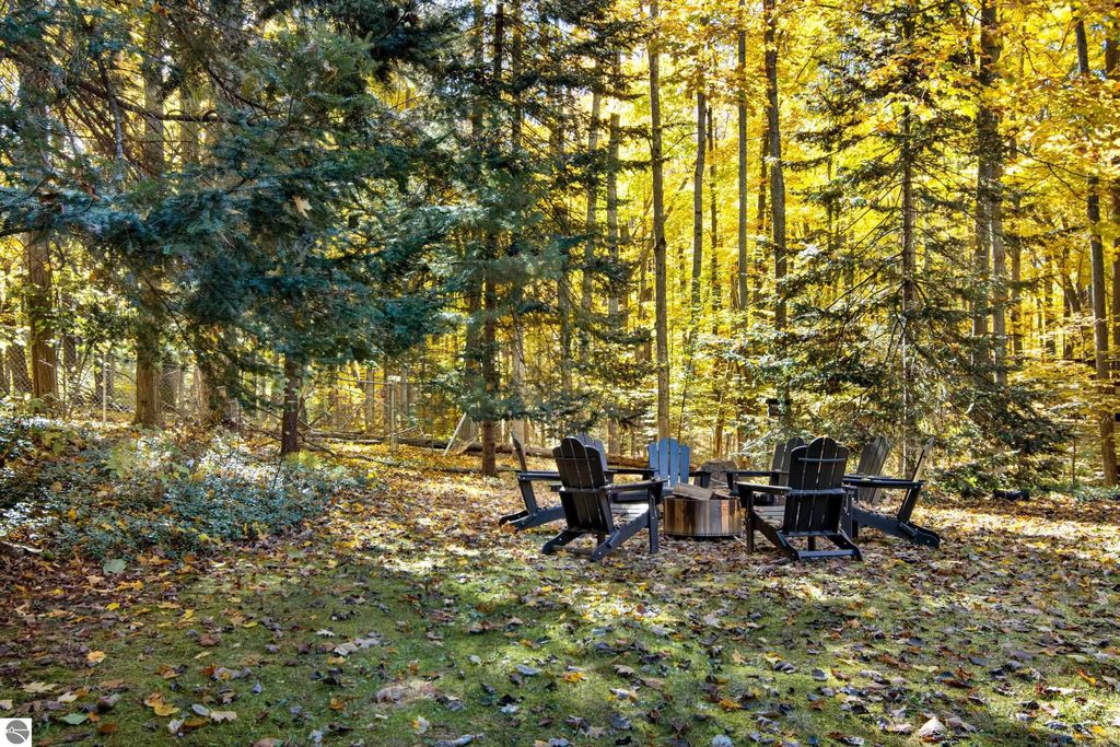 Cozy firepit area surrounded by colorful autumn foliage and wooden chairs, highlighting outdoor living space at 10371 Deerpath North, Traverse City, MI.