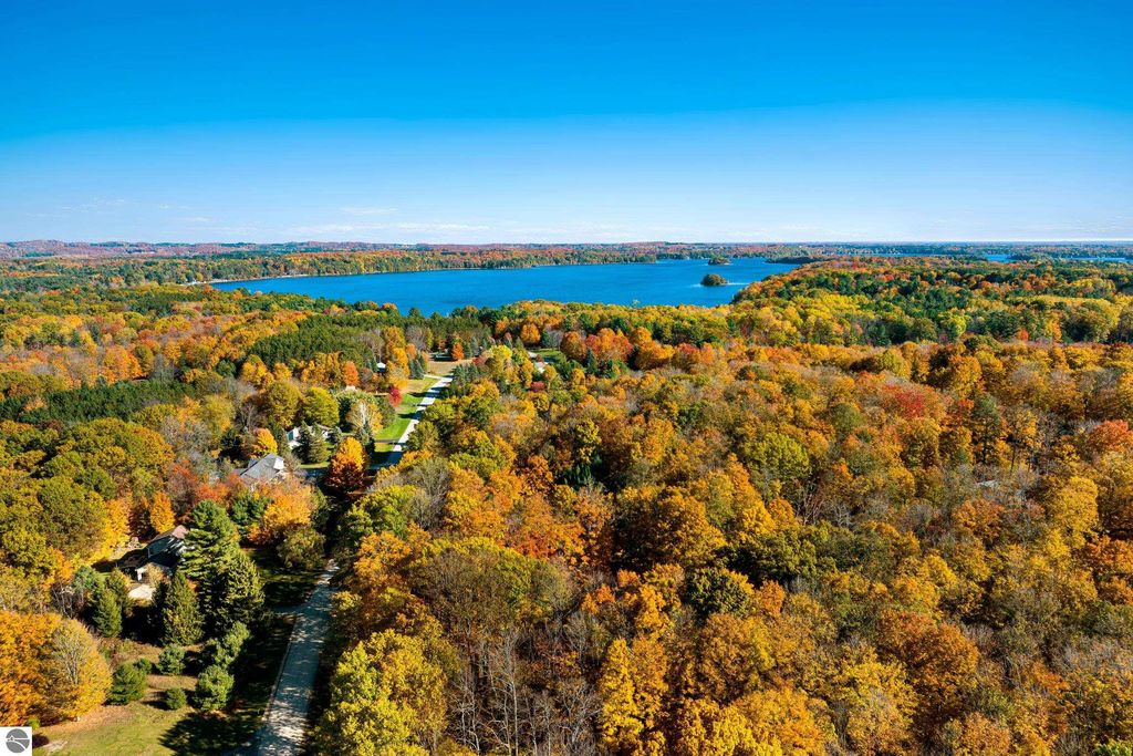 Aerial view of vibrant autumn foliage surrounding Long Lake, showcasing wooded areas and residential properties near 10371 Deerpath North in Traverse City, MI.