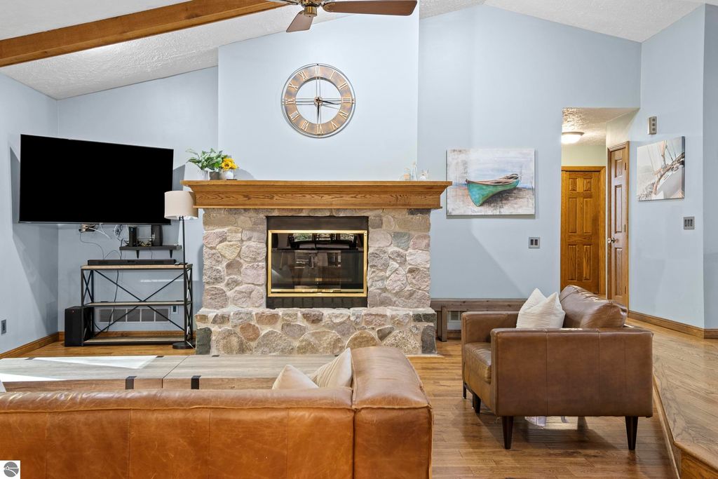 Living room interior of 10371 Deerpath North featuring a stone fireplace, wooden mantel, wall-mounted television, and modern decor, highlighting a cozy and inviting atmosphere.