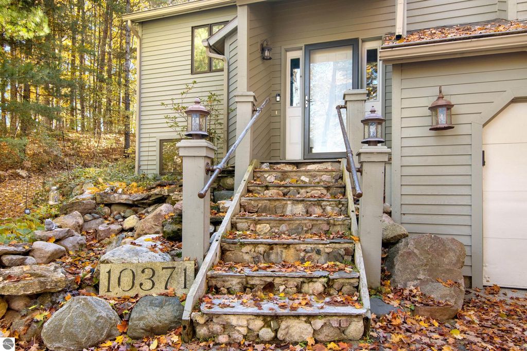 Front entrance of 10371 Deerpath North, featuring stone steps, decorative lanterns, and surrounded by autumn foliage in Traverse City, MI.