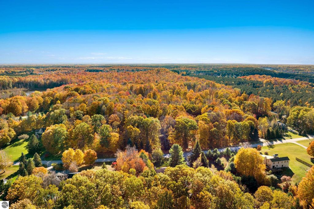 Aerial view of vibrant autumn foliage in Traverse City, Michigan, showcasing wooded landscape and nearby residential areas, emphasizing natural beauty and serene surroundings.