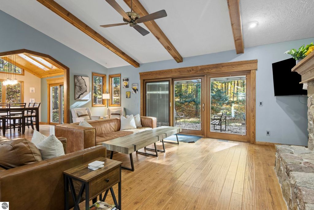 Spacious living area with wooden beams, large windows, and modern furnishings, showcasing a connection to nature at 10371 Deerpath North, Traverse City, MI.
